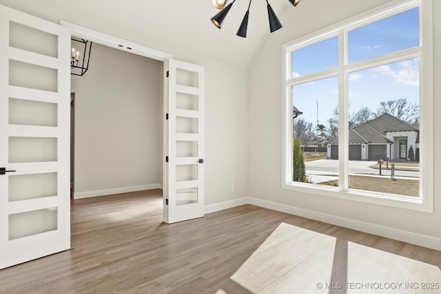 spare room with lofted ceiling, built in shelves, ceiling fan with notable chandelier, wood finished floors, and baseboards