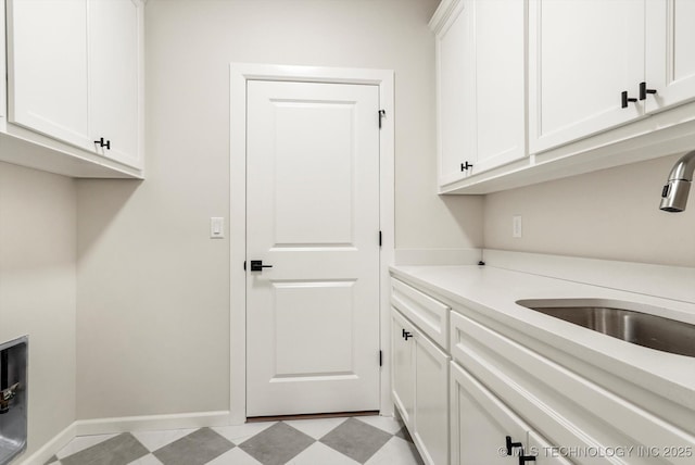 clothes washing area featuring cabinet space, baseboards, light floors, and a sink