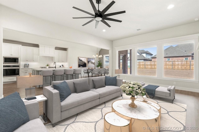 living area with light wood finished floors, baseboards, ceiling fan with notable chandelier, and recessed lighting