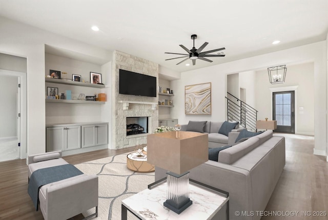 living area with recessed lighting, light wood-style flooring, built in shelves, and a stone fireplace