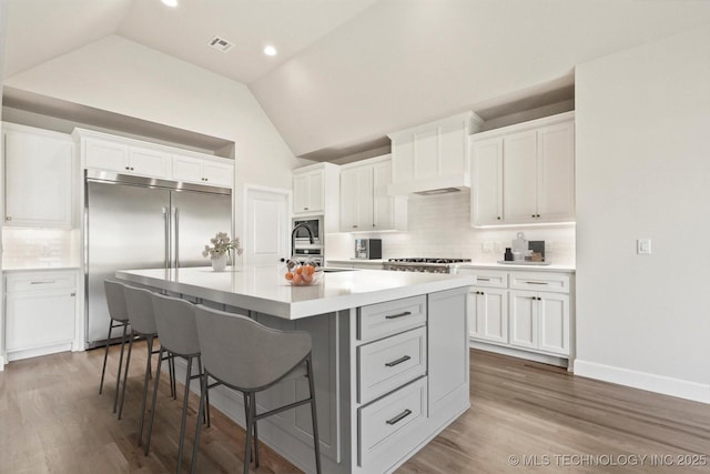 kitchen with lofted ceiling, a kitchen island with sink, wood finished floors, visible vents, and stainless steel built in refrigerator