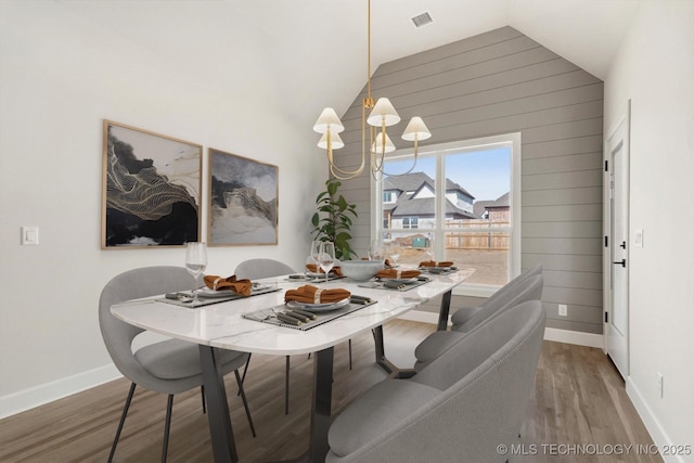 dining space featuring wooden walls, baseboards, wood finished floors, vaulted ceiling, and a chandelier