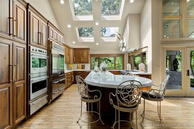 kitchen with stainless steel double oven, a kitchen island, a skylight, high vaulted ceiling, and a breakfast bar