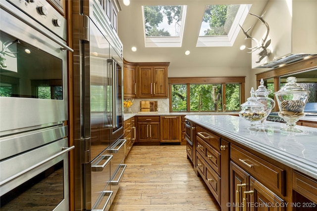 kitchen with light stone countertops, appliances with stainless steel finishes, wall chimney range hood, decorative backsplash, and light wood-type flooring