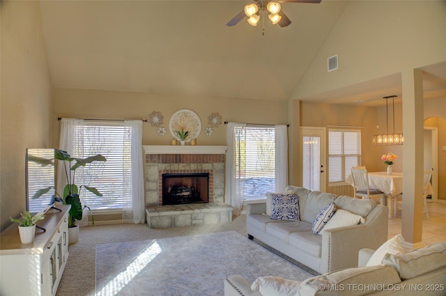 carpeted living room with ceiling fan with notable chandelier, a stone fireplace, and high vaulted ceiling