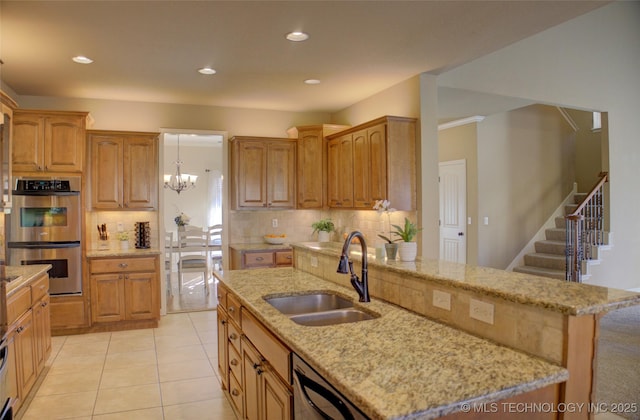 kitchen with backsplash, sink, hanging light fixtures, an island with sink, and stainless steel double oven