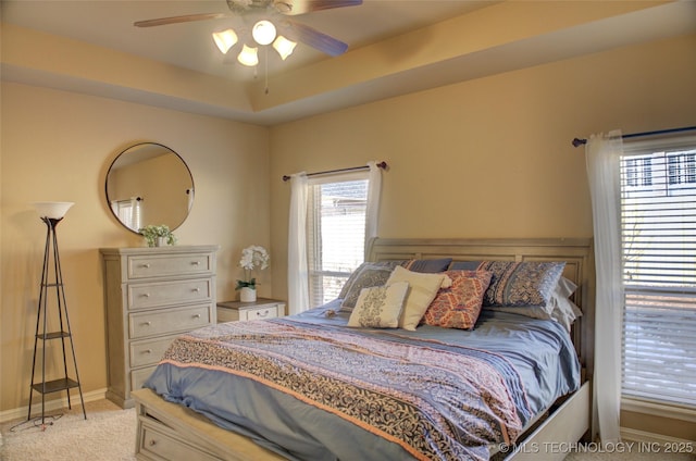 carpeted bedroom with ceiling fan and a tray ceiling