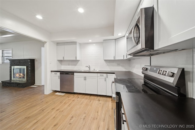 kitchen featuring a fireplace, light hardwood / wood-style floors, sink, stainless steel appliances, and white cabinets