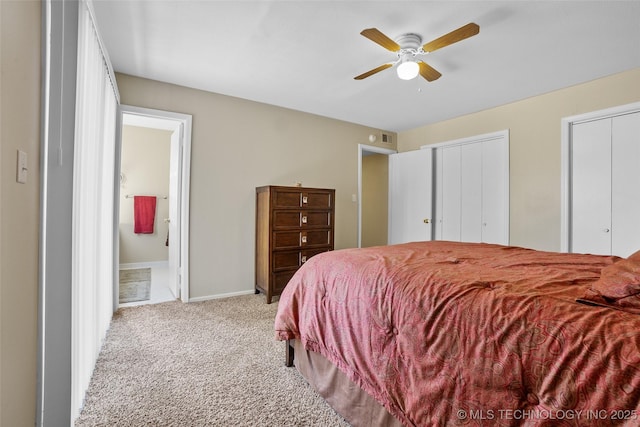 carpeted bedroom featuring ceiling fan, ensuite bathroom, and two closets