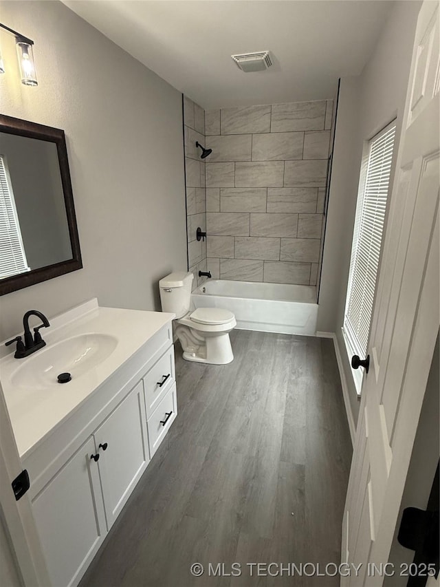 full bathroom with toilet, tiled shower / bath, hardwood / wood-style flooring, and vanity