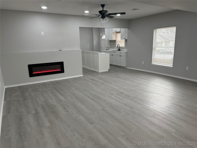 unfurnished living room with ceiling fan, sink, and light hardwood / wood-style floors