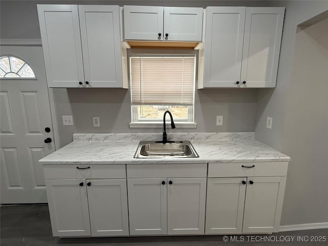 kitchen with white cabinetry, light stone counters, and sink