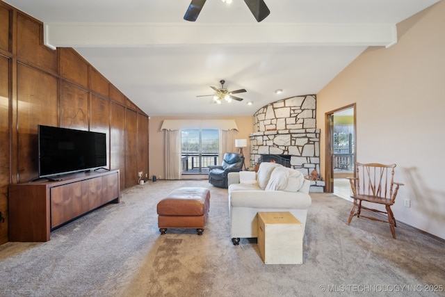 carpeted living room featuring ceiling fan, wooden walls, a stone fireplace, and vaulted ceiling with beams