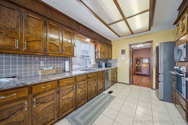 kitchen featuring sink, light tile patterned floors, appliances with stainless steel finishes, dark stone counters, and decorative backsplash