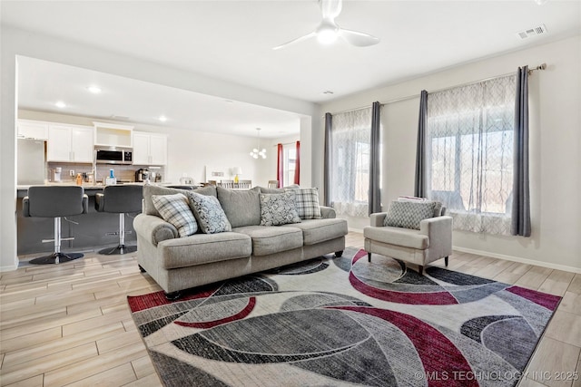 living room featuring ceiling fan with notable chandelier and light hardwood / wood-style flooring