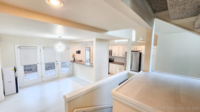 interior space with a notable chandelier, decorative backsplash, white cabinetry, hanging light fixtures, and stainless steel appliances