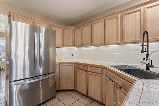 kitchen featuring light tile patterned floors, tile countertops, backsplash, stainless steel refrigerator, and sink