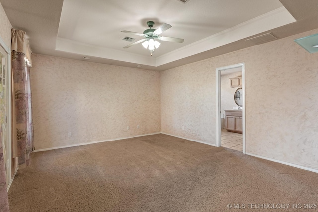 unfurnished bedroom with connected bathroom, ceiling fan, light colored carpet, a tray ceiling, and crown molding