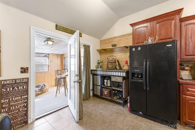 kitchen featuring black fridge with ice dispenser, light tile patterned flooring, lofted ceiling, and wooden walls