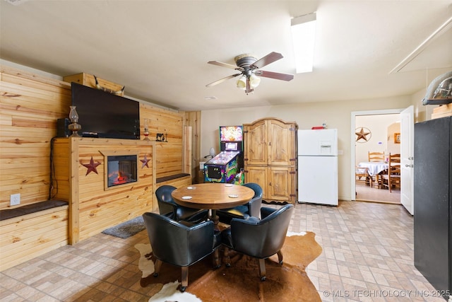 dining area featuring ceiling fan and wood walls