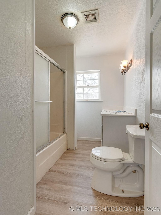 full bathroom featuring toilet, wood-type flooring, a textured ceiling, vanity, and enclosed tub / shower combo