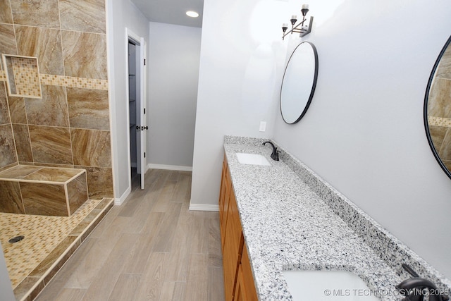 bathroom with hardwood / wood-style flooring, vanity, and a tile shower