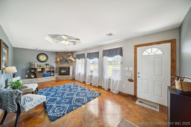 foyer entrance with ceiling fan, tile patterned floors, and a fireplace