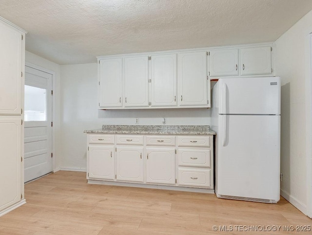 kitchen featuring white cabinetry, light hardwood / wood-style floors, light stone countertops, a textured ceiling, and white refrigerator