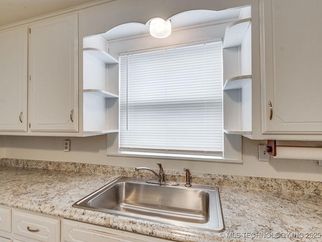 kitchen with white cabinetry, light stone counters, and sink