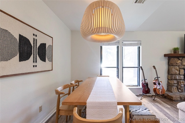 dining room featuring a healthy amount of sunlight, a stone fireplace, and hardwood / wood-style floors