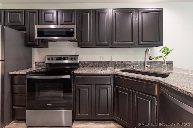 kitchen featuring light hardwood / wood-style floors, appliances with stainless steel finishes, dark stone countertops, dark brown cabinetry, and sink