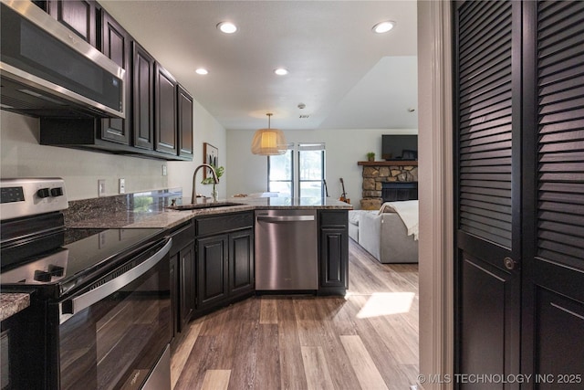 kitchen featuring light hardwood / wood-style floors, pendant lighting, sink, a stone fireplace, and stainless steel appliances