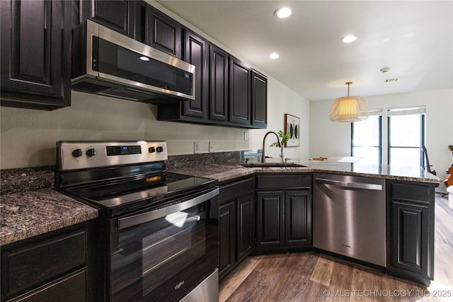 kitchen featuring decorative light fixtures, kitchen peninsula, sink, dark wood-type flooring, and appliances with stainless steel finishes