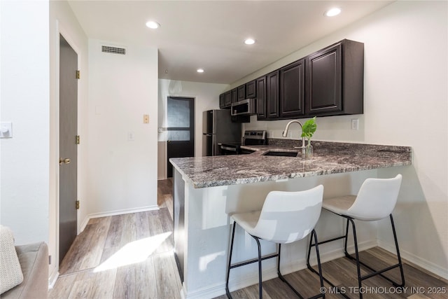 kitchen with light hardwood / wood-style floors, kitchen peninsula, appliances with stainless steel finishes, dark stone counters, and sink