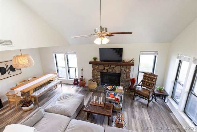 living room with ceiling fan, hardwood / wood-style floors, high vaulted ceiling, and a stone fireplace