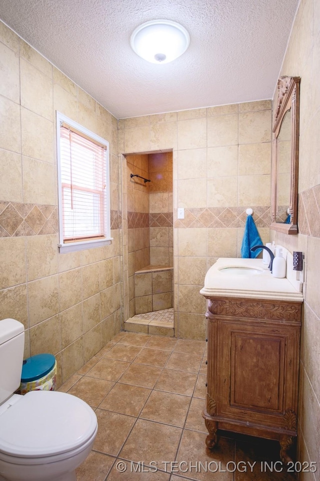 bathroom featuring toilet, a tile shower, tile walls, a textured ceiling, and vanity