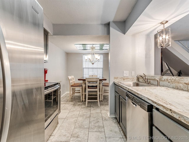 kitchen with pendant lighting, appliances with stainless steel finishes, sink, a chandelier, and light stone counters