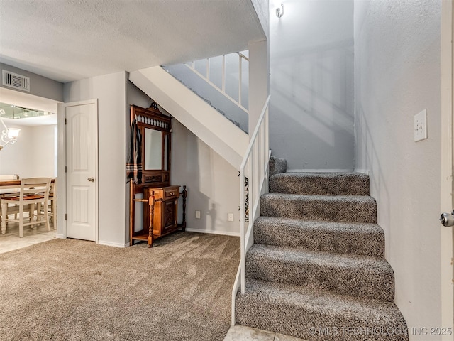 staircase featuring an inviting chandelier, a textured ceiling, and carpet flooring