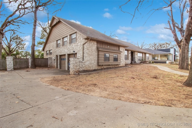 view of front facade with driveway, stone siding, a garage, and fence