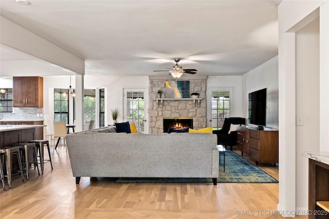 living room with light wood-type flooring, ceiling fan, and a stone fireplace