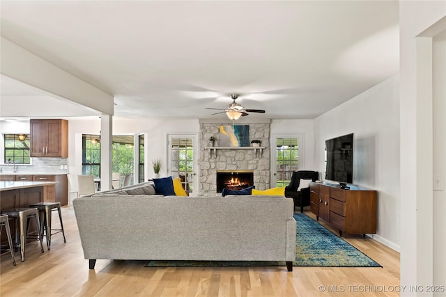 living room featuring a stone fireplace, light wood finished floors, and plenty of natural light