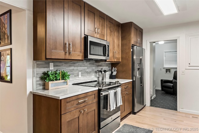 kitchen with stainless steel appliances, tasteful backsplash, light wood-style floors, light stone countertops, and baseboards