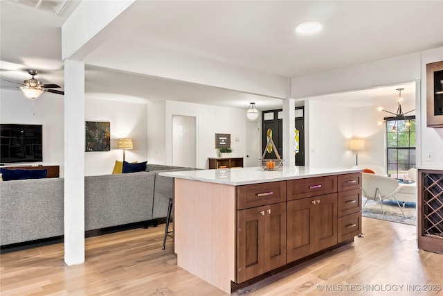 kitchen featuring ceiling fan with notable chandelier, a kitchen island, visible vents, open floor plan, and light wood-type flooring