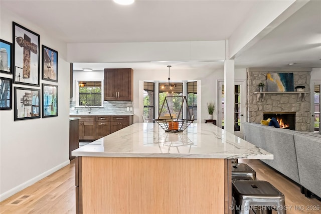 kitchen featuring decorative backsplash, open floor plan, a center island, light stone countertops, and light wood-type flooring