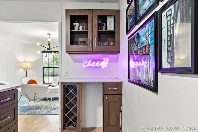 bar with light wood-style floors, beverage cooler, and an inviting chandelier