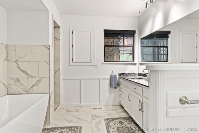 bathroom featuring a washtub, a decorative wall, a wainscoted wall, vanity, and marble finish floor