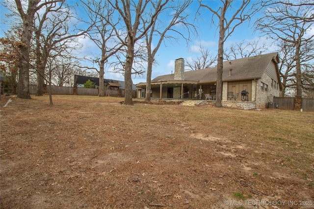 back of house featuring stone siding, a chimney, fence, and a lawn