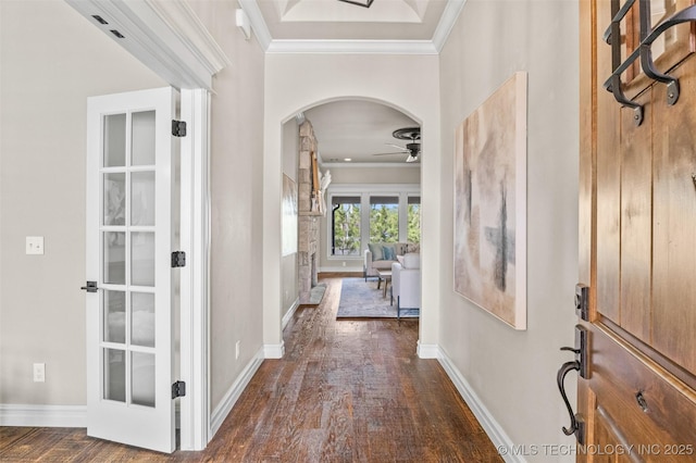 foyer entrance with baseboards, arched walkways, dark wood-style flooring, a ceiling fan, and crown molding
