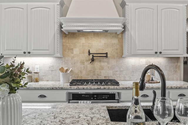 kitchen with white cabinets, custom exhaust hood, appliances with stainless steel finishes, light stone counters, and decorative backsplash