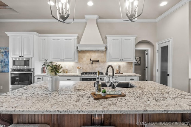 kitchen featuring white cabinetry, appliances with stainless steel finishes, premium range hood, and an inviting chandelier